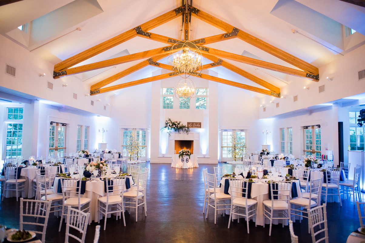 A wedding reception at The Manor House in a large room with white and blue tables and chandeliers.