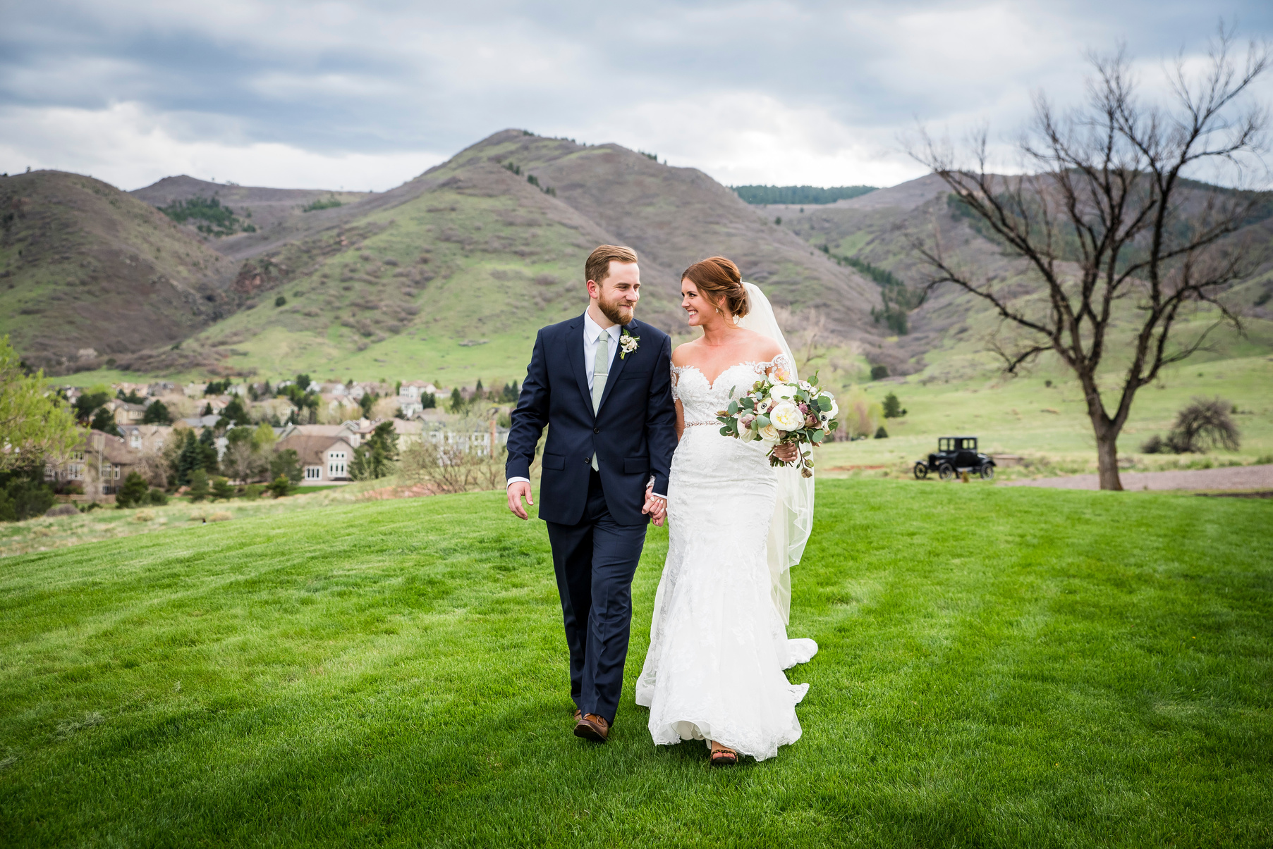 A bride and groom walking on the grass in front of the mountains at The Manor House in Littleton, Colorado.