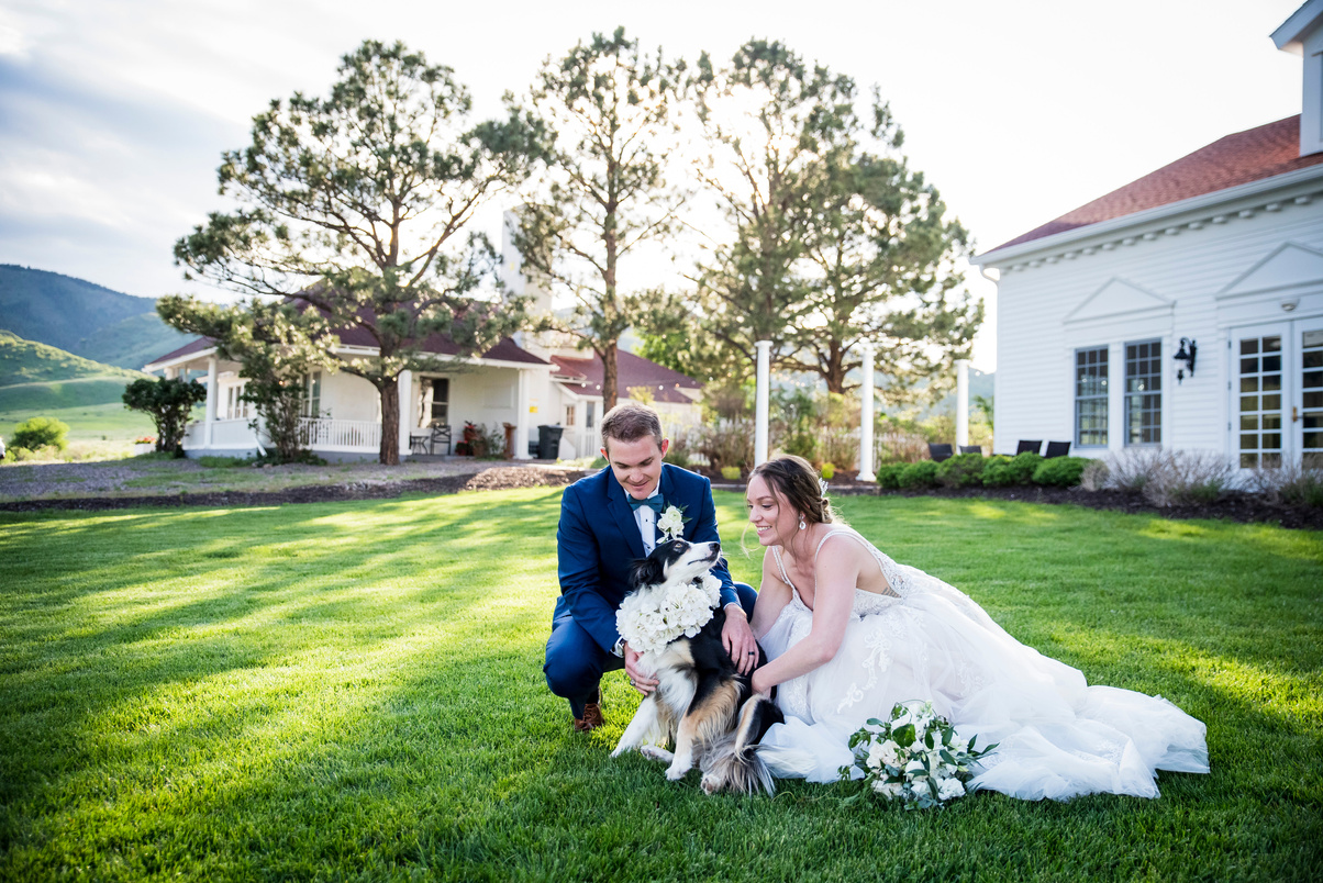 A bride and groom pose with their dog in the lawn at The Manor House, captured by Denver wedding photographer, Two One Photography.