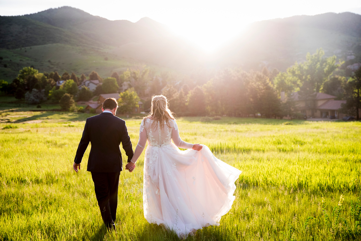 A bride and groom walking away from the camera in a field at sunset at The Manor House in Littleton, Colorado.