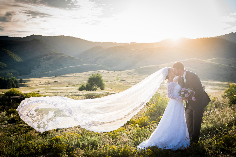 A bride and groom in the mountains at sunset with her wedding veil blowing in the wind.