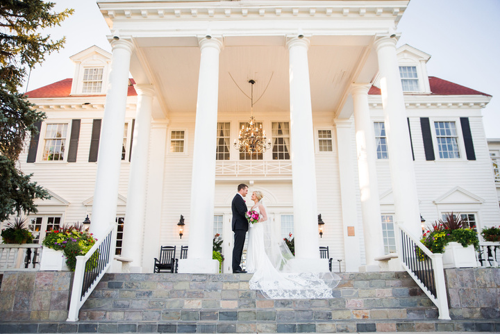 A bride and groom on steps in front of The Manor House in Littleton, Colorado.