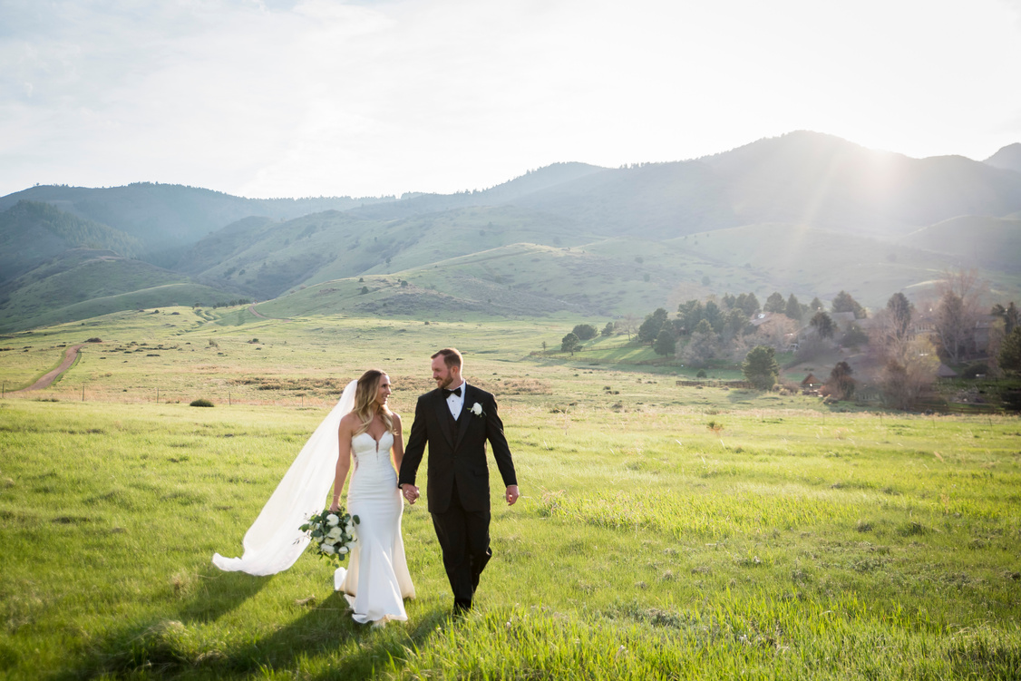 A bride and groom walking in a field with mountains in the background at The Manor House in Littleton, Colorado.